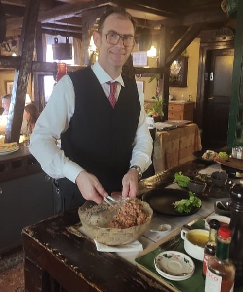 Portrait de François Morand, propriétaire du restaurant La Diligence à Saint-Louis, en train de préparer le Steak Tartare à la table du client.